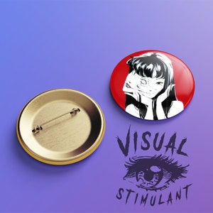 May include: A black and white illustration of a woman with long black hair covering her face with a hand. The illustration is on a red background. The pin is a round button with a gold metal back.