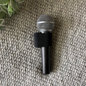 May include: A black microphone with a silver mesh head and a black foam windscreen. The microphone is on a gray textured surface.