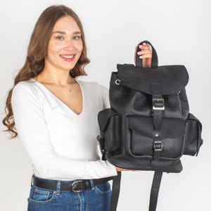 May include: A black leather backpack with multiple pockets and a buckle closure. The backpack has a drawstring closure at the top.