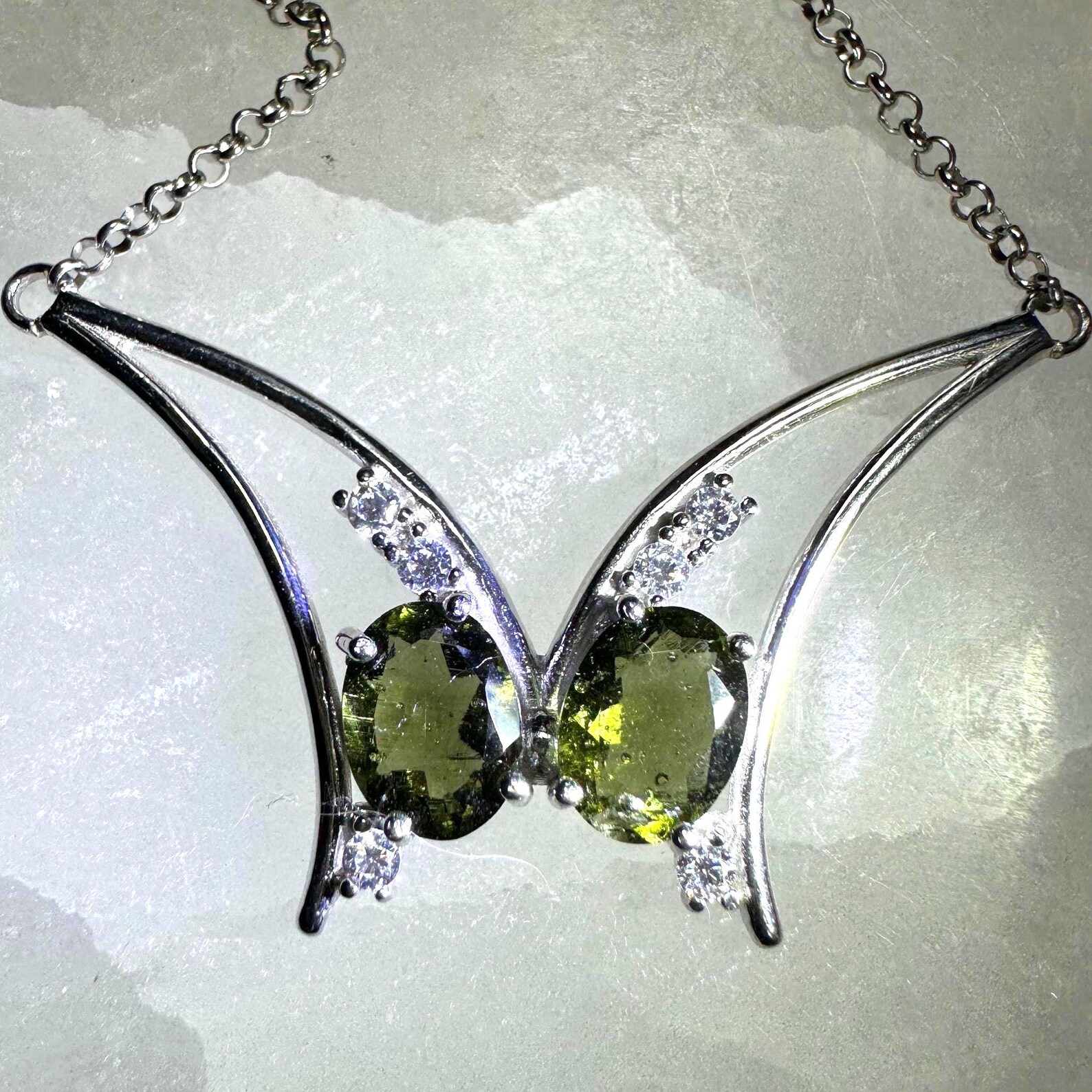 Butterfly-shaped necklace featuring twin oval moldavite gemstones and cubic zirconia accents set in polished sterling silver.