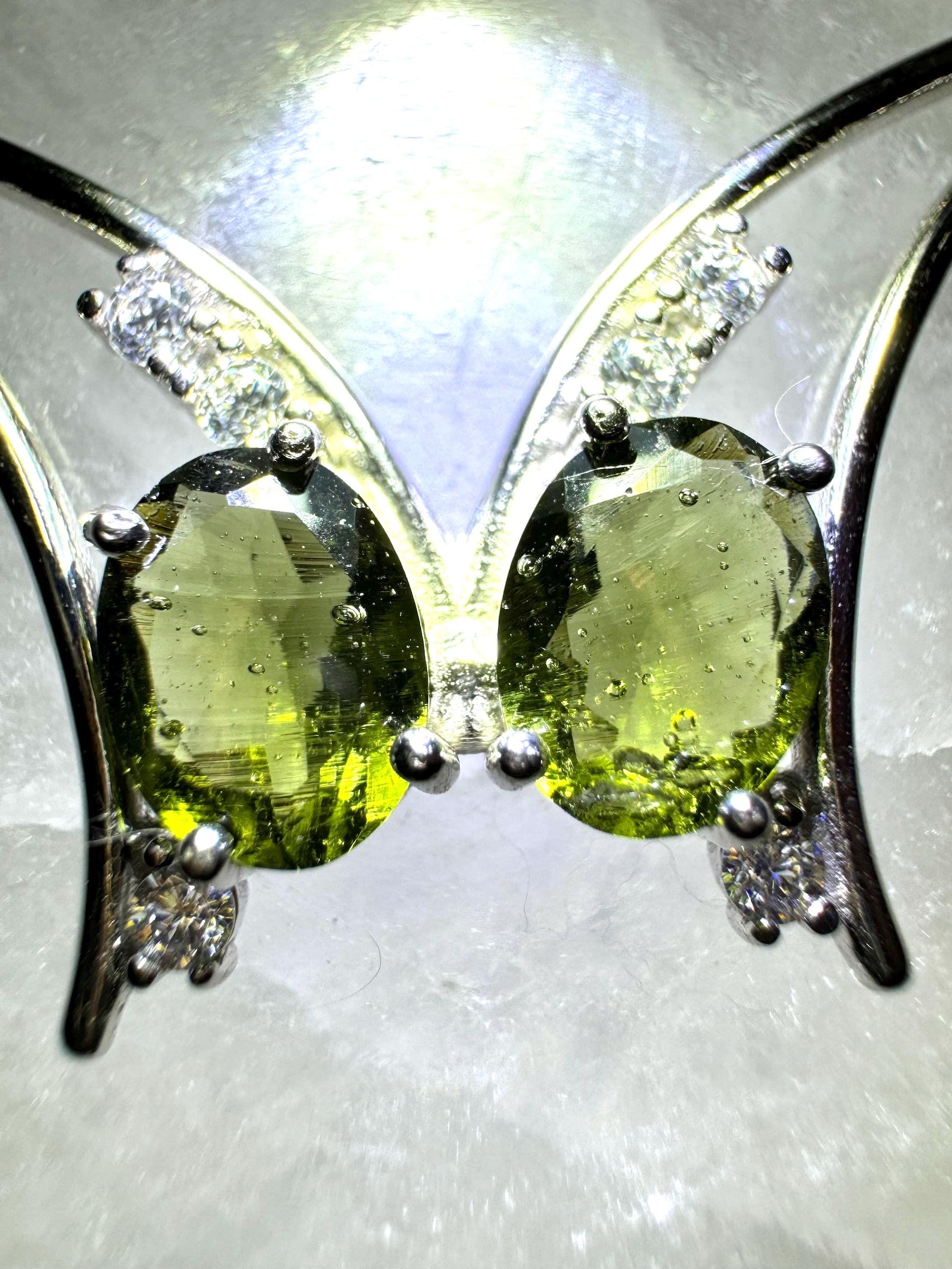 Close-up of butterfly pendant showcasing two faceted moldavite stones with cubic zirconia gems set in sterling silver.