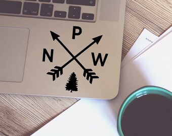 May include: Black and white sticker with a compass design featuring arrows pointing north, west, east, and south. The compass is centered around a small pine tree.