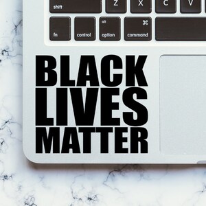 May include: A laptop computer with a black sticker that reads "Black Lives Matter" on the trackpad.