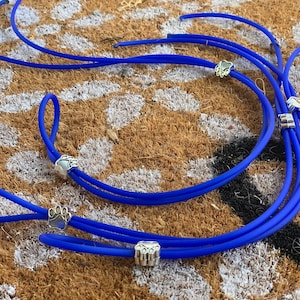 May include: Blue silicone cord with silver paw print charms. The cord is looped and coiled on a brown surface.