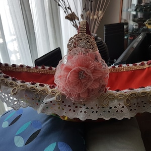 以下が含まれることがあります： 赤と白のギフトバスケットにピンクの花と金の縁取りが施されています。バスケットはレースとラインストーンで飾られています。