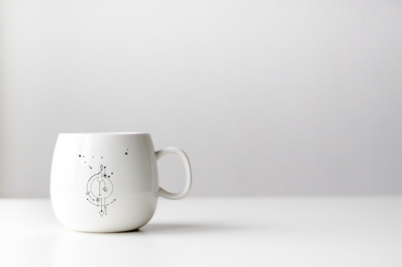 Pu&ograve; includere: Una tazza in ceramica bianca con un design geometrico in bianco e nero di una costellazione sul lato.