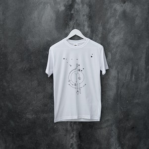 Pu&ograve; includere: Maglietta bianca con un design geometrico stampato sul davanti. Il design presenta un cerchio con una serie di linee e forme all'interno, tra cui un triangolo, un quadrato e un cerchio.