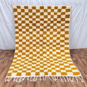 Puede incluir: Una alfombra grande y rectangular con un patrón de cuadros en amarillo mostaza y blanco. La alfombra tiene un borde de flecos.