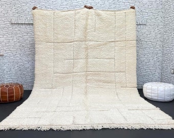 May include: A white Moroccan rug with a geometric pattern. The rug has a fringe border and is made of wool.