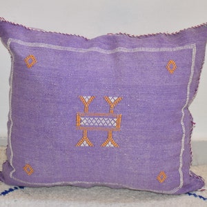 May include: Purple throw pillow with a white and orange embroidered design. The pillow has a zipper closure.