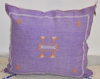 May include: Purple throw pillow with a white and orange embroidered design. The pillow has a zipper closure.