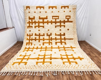 May include: A white and mustard yellow geometric patterned rug with fringe. The rug has a modern design with a bold geometric pattern.