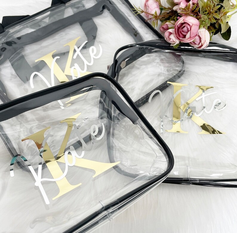 May include: Three clear plastic zippered bags with black trim. Each bag has a gold letter "K" and the name "Kate" written in white on the front.