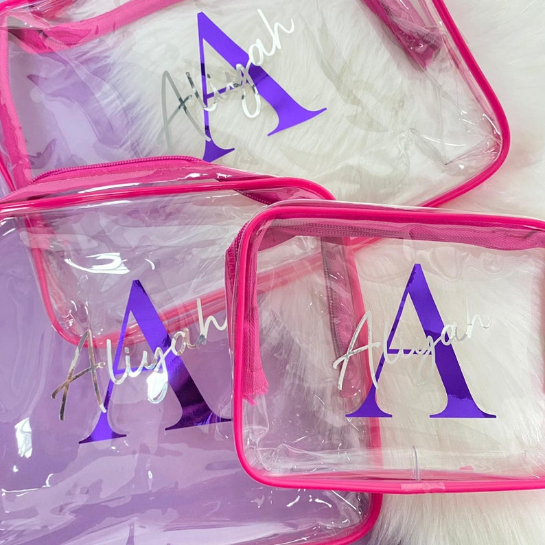 May include: Three clear plastic zippered pouches with pink trim. Each pouch has a personalized name, "Aliyah", written in silver with a purple letter "A".