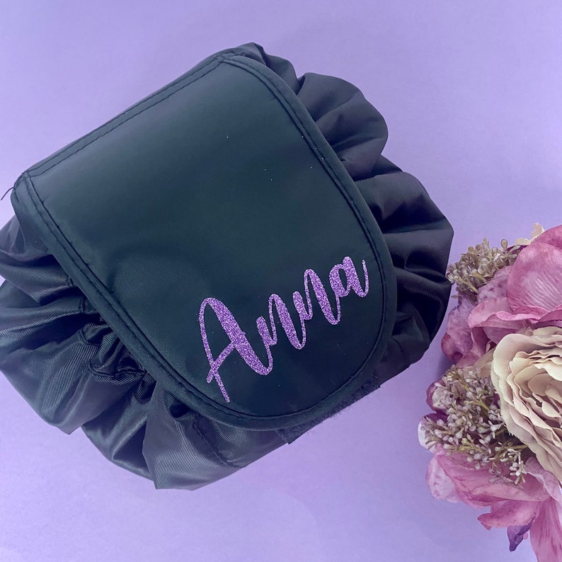 May include: A black drawstring makeup bag with a purple glitter name "Anna" on the front.
