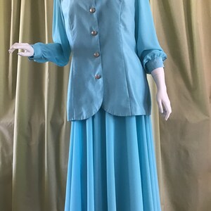 May include: A light blue two-piece outfit consisting of a long-sleeved button-up top and a flowing skirt. The top features silver buttons and the skirt has a wide, flowing silhouette.