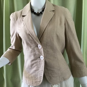 May include: A beige blazer with a striped pattern and two white buttons. The blazer has a notched collar and long sleeves.
