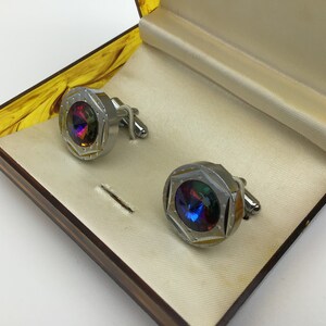 May include: A pair of silver cufflinks with iridescent blue and green gemstones in a yellow box.