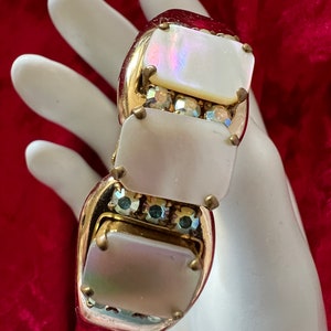 May include: A gold tone bracelet with three rectangular white mother of pearl stones set in gold tone bezels. Each stone is accented with clear and iridescent rhinestones.