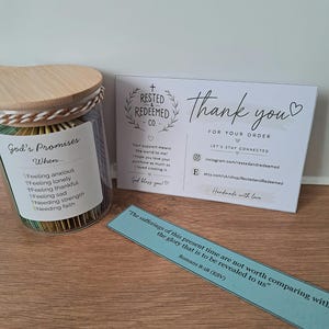 May include: A glass jar with a wooden lid, filled with colourful paper strips, labelled "God's Promises." A thank you card and a blue bookmark with text are also present. The jar's label lists feelings and needs.