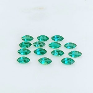 May include: A collection of 15 marquise-shaped green gemstones, arranged in a staggered pattern on a white surface.