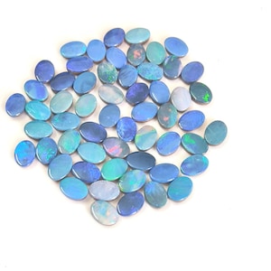 May include: A collection of numerous oval-shaped blue opals, each displaying iridescent flashes of green, pink, and light blue. These polished gemstones are arranged in a loose cluster, showcasing varied shades of deep and sky blue.