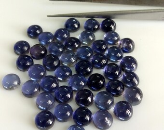May include: A collection of 40 round, cabochon cut, blue gemstones. The stones are smooth and polished, with a translucent appearance. They are arranged in a loose pile on a white surface.