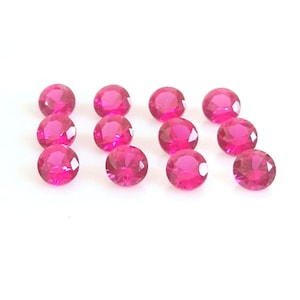 May include: Twelve round, faceted, pink gemstones on a white background.