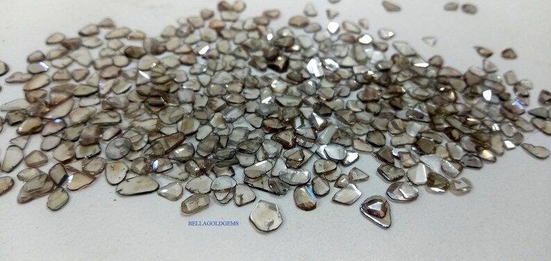 May include: A pile of rough, unpolished, brown diamonds, also known as raw diamonds. The diamonds are various shapes and sizes, with some having a slight iridescent sheen.
