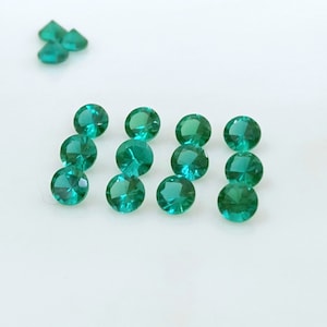 May include: Ten round, faceted, green gemstones. The gemstones are arranged in a row on a white surface.