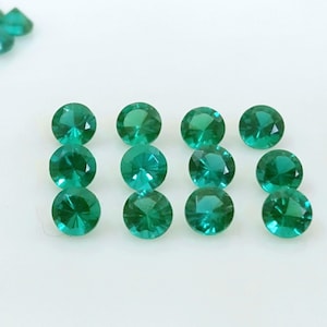 May include: Twelve round, faceted, green gemstones on a white surface.