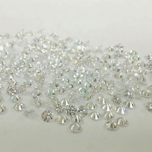 May include: A collection of small, sparkling diamonds scattered on a white surface. The diamonds vary in size and shape, reflecting light and creating a brilliant display. Ideal for jewelry making or other crafts.