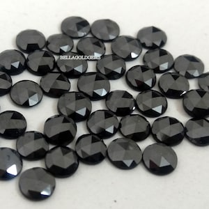 Puede incluir: Una colección de 30 piedras preciosas redondas facetadas negras. Las piedras preciosas están sueltas y dispersas sobre una superficie blanca.