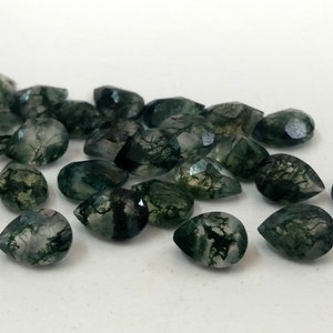 May include: A collection of green moss agate pear-shaped gemstones. The stones are translucent and have a variety of green and white patterns.