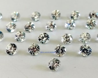 Pode incluir: Uma coleção de 40 gemas redondas, transparentes e facetadas. As gemas estão dispostas em forma de semicírculo sobre uma superfície branca.