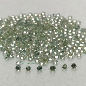 May include: A large pile of small, round, green and clear gemstones. The gemstones are scattered on a white surface.