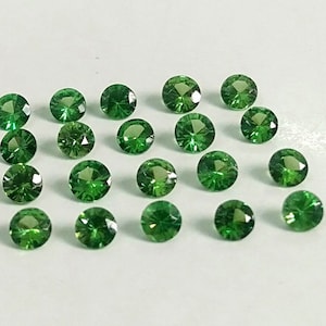 May include: Twenty green gemstones, each with a round, faceted shape, are arranged in a staggered pattern on a white surface.
