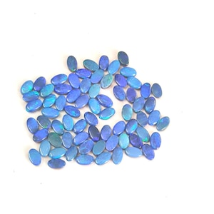 May include: A collection of numerous small, oval-shaped blue opals. Each gemstone displays a smooth, polished surface with iridescent flashes of light blue, dark blue, and hints of green throughout the stones, arranged in a loose cluster.