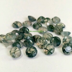 Könnte beinhalten: Eine Sammlung von 18 runden, facettierten Moosachat-Edelsteinen. Die Steine sind eine Mischung aus Grün und Weiß mit einem durchscheinenden Aussehen. Die Steine haben einen Durchmesser von etwa 6 mm.