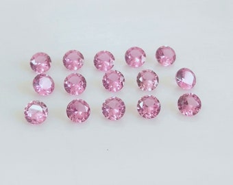 Puede incluir: Una colección de 16 piedras preciosas redondas de color rosa. Las piedras preciosas están dispuestas en filas sobre una superficie blanca.