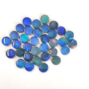 May include: A collection of round, flat, polished opals featuring a deep blue base colour with iridescent flashes of green, teal, and occasional orange. Each stone displays a smooth, circular shape with a reflective surface that catches light.
