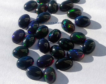 May include: A collection of 20 oval-shaped black opals with iridescent green, blue, and red flashes. The opals are scattered on a white surface.