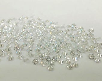 May include: A collection of small, sparkling diamonds scattered on a white surface. The diamonds vary in size and shape, reflecting light and creating a brilliant display. Ideal for jewelry making or other crafts.