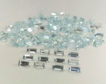 May include: A collection of light blue aquamarine gemstones in a rectangular baguette cut. The gemstones are arranged in a pile and a row.