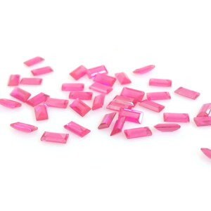 Könnte beinhalten: Eine Streuung von rechteckigen rosa Edelsteinen auf weißem Hintergrund.