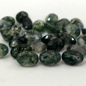 May include: A collection of oval-shaped green moss agate gemstones. The stones have a translucent green colour with dark green moss-like inclusions.