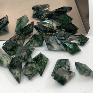 May include: A collection of 20 green moss agate gemstone cabochons in a kite shape. The stones are translucent and have a variety of green and white patterns.