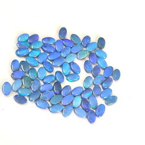 May include: A collection of numerous oval-shaped blue opals arranged in a loose cluster. Each gemstone displays a smooth, polished surface with iridescent flashes of light, primarily in shades of deep blue, cyan, and hints of green throughout.