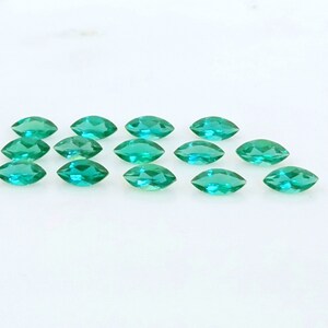May include: A collection of 14 marquise-shaped green gemstones, arranged in two rows on a white surface.