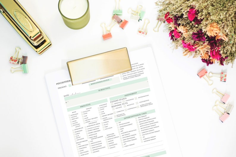 May include: A white clipboard with a green and white checklist for a psychotherapy session. The checklist includes sections for objective, subjective, assessment, interventions used, and notes. The clipboard is on a white surface with a gold stapler, a candle, and a bouquet of dried flowers.